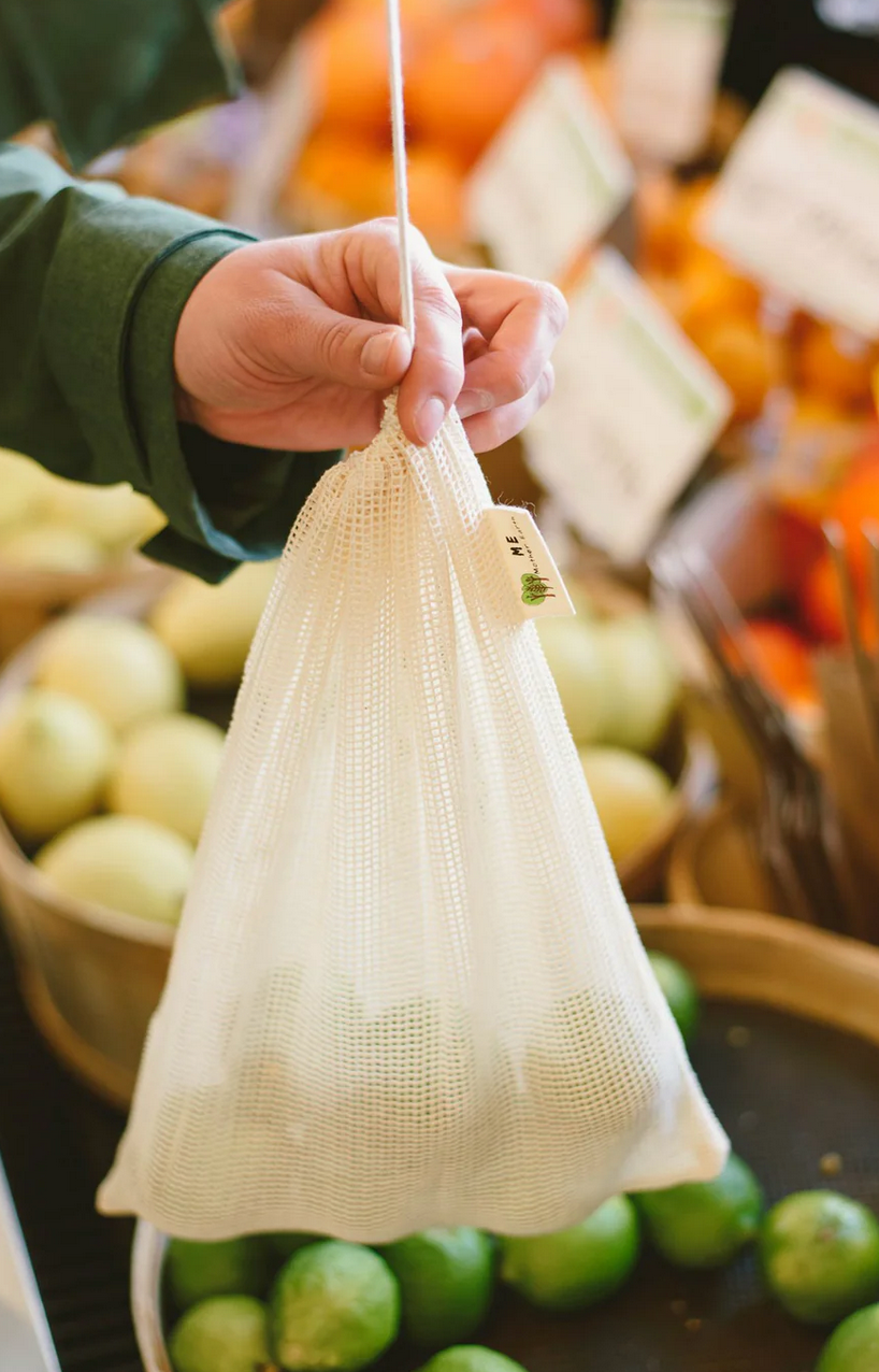 Hand holding a white mesh produce bag with green apples in the background